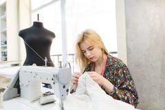 Näherinmädchen sitzt am Arbeitsplatz nahe einer Nähmaschine und näht einen weißen Stoff mit ihren Händen stockbild Näherinmädchen sitzt am Arbeitsplatz nahe einer Nähmaschine und näht einen weißen Stoff mit ihren Händen stockbild