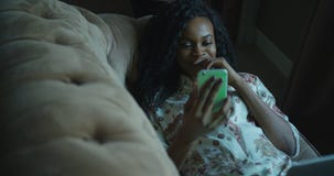 Närbildsikt av den gladlynta unga afro--amerikan kvinnan som skrattar och pratar genom att använda mobiltelefonen, medan ligga på lager videofilmer Närbildsikt av den gladlynta unga afro--amerikan kvinnan som skrattar och pratar genom att använda mobiltelefonen, medan ligga på lager videofilmer