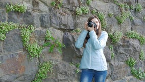 Nätt ung flicka som tar foto med en yrkesmässig kamera Tappningvägg av den lösa stenen i bakgrunden stock video Nätt ung flicka som tar foto med en yrkesmässig kamera Tappningvägg av den lösa stenen i bakgrunden stock video
