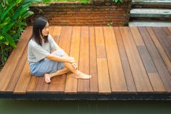 O assento asiático da mulher relaxa no terraço ou no patamar de madeira perto da lagoa no jardim fotos de stock O assento asiático da mulher relaxa no terraço ou no patamar de madeira perto da lagoa no jardim fotos de stock