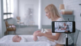 O blogger da mamã faz a ginástica para sua pouca filha na tabela em mudança e registros video para subscritores em social video estoque O blogger da mamã faz a ginástica para sua pouca filha na tabela em mudança e registros video para subscritores em social video estoque