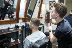 O cabeleireiro mostra o corte de cabelo curto com o espelho ao cliente satisfeito considerável no salão de beleza profissional do imagens de stock royalty free O cabeleireiro mostra o corte de cabelo curto com o espelho ao cliente satisfeito considerável no salão de beleza profissional do imagens de stock royalty free