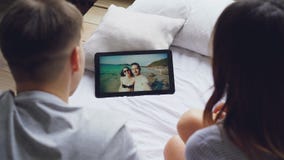 O casal está falando aos amigos no skype usando a tabuleta, os amantes felizes são de riso e de beijo na tela com vídeos de arquivo O casal está falando aos amigos no skype usando a tabuleta, os amantes felizes são de riso e de beijo na tela com vídeos de arquivo