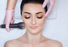 O cosmetologist faz ao procedimento uma limpeza ultrassônica da pele facial de um bonito, jovem mulher em um salão de beleza foto de stock royalty free O cosmetologist faz ao procedimento uma limpeza ultrassônica da pele facial de um bonito, jovem mulher em um salão de beleza foto de stock royalty free