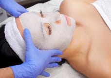 O cosmetologist para o procedimento de limpar e de hidratar a pele, aplicando uma máscara da folha à cara de uma jovem mulher no imagens de stock royalty free O cosmetologist para o procedimento de limpar e de hidratar a pele, aplicando uma máscara da folha à cara de uma jovem mulher no imagens de stock royalty free