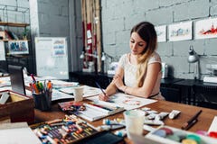 O desenho fêmea novo focalizado do artista esboça usando os lápis coloridos que sentam-se em sua oficina à moda fotografia de stock royalty free O desenho fêmea novo focalizado do artista esboça usando os lápis coloridos que sentam-se em sua oficina à moda fotografia de stock royalty free