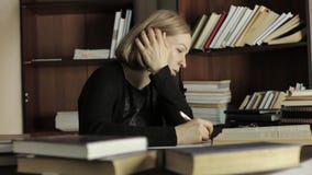 O estudante fêmea que senta-se na mesa e redige para fora a informação necessária do livro vídeos de arquivo O estudante fêmea que senta-se na mesa e redige para fora a informação necessária do livro vídeos de arquivo
