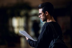 O estudante novo da informática consulta alguns papéis iluminados pela luz de uma tela em um corredor fotos de stock royalty free O estudante novo da informática consulta alguns papéis iluminados pela luz de uma tela em um corredor fotos de stock royalty free