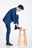 O estúdio disparou de um homem de negócios asiático novo que veste um laço que levanta seu pé em uma cadeira imagens de stock royalty free O estúdio disparou de um homem de negócios asiático novo que veste um laço que levanta seu pé em uma cadeira imagens de stock royalty free