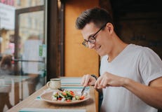 O homem caucasiano novo com vidros que come uma salada saudável fotografia de stock O homem caucasiano novo com vidros que come uma salada saudável fotografia de stock
