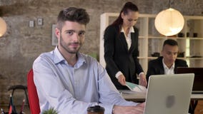 O homem de negócios novo está olhando o portátil no escritório, olhando na câmera, sorrindo, pessoa é trabalhos em rede com tecno video estoque O homem de negócios novo está olhando o portátil no escritório, olhando na câmera, sorrindo, pessoa é trabalhos em rede com tecno video estoque