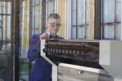 O homem em um terno azul olha a máquina impressora atrás do vidro imagens de stock royalty free O homem em um terno azul olha a máquina impressora atrás do vidro imagens de stock royalty free