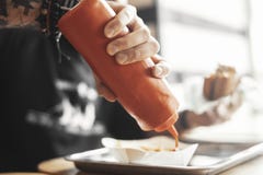 O homem farpado novo do moderno derrama a ketchup em batatas fritas perto acima imagens de stock O homem farpado novo do moderno derrama a ketchup em batatas fritas perto acima imagens de stock