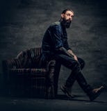O homem farpado Tattooed senta-se em uma cadeira imagem de stock O homem farpado Tattooed senta-se em uma cadeira imagem de stock