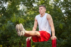O homem forte novo balança a imprensa em uma barra horizontal em uma terra de esportes no verão na cidade fotos de stock royalty free O homem forte novo balança a imprensa em uma barra horizontal em uma terra de esportes no verão na cidade fotos de stock royalty free