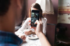 O homem fotografa a menina no café amor e tecnologia imagem de stock O homem fotografa a menina no café amor e tecnologia imagem de stock