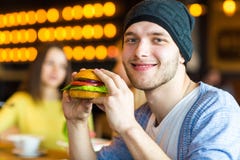 O homem nas mãos guarda um hamburguer Antropófago um hamburguer no café imagem de stock royalty free O homem nas mãos guarda um hamburguer Antropófago um hamburguer no café imagem de stock royalty free