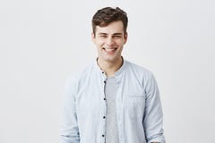 O homem novo atrativo considerável vestiu-se na luz - camisa azul sobre o t-shirt com cabelo escuro e looknig atraente dos olhos fotos de stock O homem novo atrativo considerável vestiu-se na luz - camisa azul sobre o t-shirt com cabelo escuro e looknig atraente dos olhos fotos de stock
