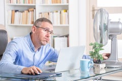 O homem sofre do calor no escritório ou em casa Imagem de Stock O homem sofre do calor no escritório ou em casa Imagem de Stock