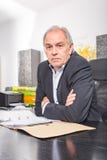 O homem superior senta-se em uma mesa, enrolando em um arquivo de original fotos de stock royalty free O homem superior senta-se em uma mesa, enrolando em um arquivo de original fotos de stock royalty free