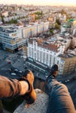 O indivíduo está sentando-se na borda de uma construção alta Pendurou seus pés com as sapatilhas pretas bonitas sobre a cidade imagens de stock O indivíduo está sentando-se na borda de uma construção alta Pendurou seus pés com as sapatilhas pretas bonitas sobre a cidade imagens de stock
