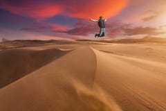 O indivíduo que salta no deserto em uma duna de areia no por do sol fotografia de stock royalty free O indivíduo que salta no deserto em uma duna de areia no por do sol fotografia de stock royalty free