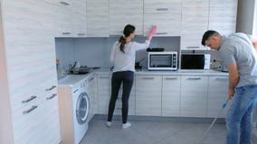 O marido e a esposa estão limpando na cozinha junto O homem lava o assoalho com um espanador e a mulher limpa a mobília O marido e a esposa estão limpando na cozinha junto O homem lava o assoalho com um espanador e a mulher limpa a mobília