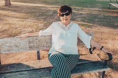O meio latino-americano bonito envelheceu a mulher no parque que senta-se em um banco no por do sol imagem de stock O meio latino-americano bonito envelheceu a mulher no parque que senta-se em um banco no por do sol imagem de stock