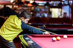 O menino bonito na camisa amarela de t joga o bilhar ou a associação no clube A criança aprende jogar a sinuca Menino com sugestã fotos de stock O menino bonito na camisa amarela de t joga o bilhar ou a associação no clube A criança aprende jogar a sinuca Menino com sugestã fotos de stock