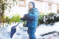 O menino caucasiano pequeno trabalha com pá a neve na jarda com os arbustos cor-de-rosa nevados bonitos Criança com jogos da pá f fotografia de stock O menino caucasiano pequeno trabalha com pá a neve na jarda com os arbustos cor-de-rosa nevados bonitos Criança com jogos da pá f fotografia de stock