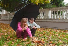 O menino e a menina sentam-se sob um guarda-chuva fotografia de stock royalty free O menino e a menina sentam-se sob um guarda-chuva fotografia de stock royalty free