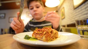 O menino está comendo uma lasanha em um café com faca e forquilha filme O menino está comendo uma lasanha em um café com faca e forquilha filme