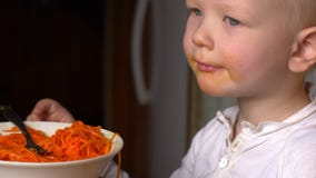 O menino louro engraçado está comendo a salada coreana da cenoura na cozinha ao lado de seu irmão As crian?as est?o felizes junto vídeos de arquivo O menino louro engraçado está comendo a salada coreana da cenoura na cozinha ao lado de seu irmão As crian?as est?o felizes junto vídeos de arquivo