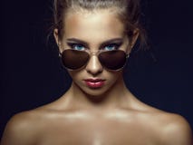 O modelo de olhos azuis bronzeado lindo com bonito compõem e o cabelo do bebê em torno de sua cara que olha sobre seus óculos de imagem de stock royalty free O modelo de olhos azuis bronzeado lindo com bonito compõem e o cabelo do bebê em torno de sua cara que olha sobre seus óculos de imagem de stock royalty free
