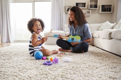 O mum preto novo joga a uquelele com filha da criança em casa fotografia de stock O mum preto novo joga a uquelele com filha da criança em casa fotografia de stock