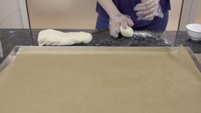 O padeiro fêmea está rolando a parte pequena de massa na tabela preta na cozinha video estoque O padeiro fêmea está rolando a parte pequena de massa na tabela preta na cozinha video estoque