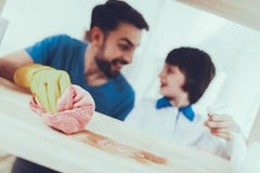 O pai e o filho limpam superfícies da mobília da poeira fotografia de stock O pai e o filho limpam superfícies da mobília da poeira fotografia de stock