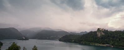 O panorama de uma manhã cinzenta e terrível nas montanhas alpinas no lago sangrou foto de stock O panorama de uma manhã cinzenta e terrível nas montanhas alpinas no lago sangrou foto de stock