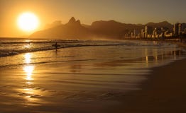 O por do sol dourado com a silhueta da montanha e do surfista de Dois Irmaos em Ipanema encalha imagens de stock royalty free O por do sol dourado com a silhueta da montanha e do surfista de Dois Irmaos em Ipanema encalha imagens de stock royalty free