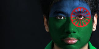 O retrato de um homem com a bandeira dos povos Romani pintou em sua cara no fundo preto imagem de stock O retrato de um homem com a bandeira dos povos Romani pintou em sua cara no fundo preto imagem de stock