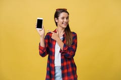 O retrato de uma moça feliz vestiu-se no verão que aponta o dedo no telefone celular da tela vazia isolado sobre o amarelo fotos de stock royalty free O retrato de uma moça feliz vestiu-se no verão que aponta o dedo no telefone celular da tela vazia isolado sobre o amarelo fotos de stock royalty free