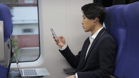 O retrato do homem de negócios coreano que está datilografando a mensagem em seu telefone celular ao viajar pelo trem video estoque O retrato do homem de negócios coreano que está datilografando a mensagem em seu telefone celular ao viajar pelo trem video estoque