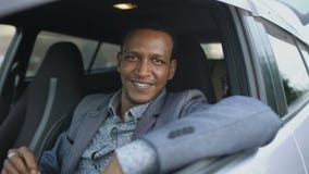 O retrato do homem de negócios sério que senta-se dentro do carro pôs dos óculos de sol e do sorriso na câmera fora O retrato do homem de negócios sério que senta-se dentro do carro pôs dos óculos de sol e do sorriso na câmera fora