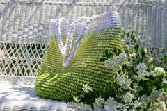 O saco verde-branco feito à mão feito malha fica no sofá de vime branco no jardim com bouqet de florescência do spirea de lado fotos de stock royalty free O saco verde-branco feito à mão feito malha fica no sofá de vime branco no jardim com bouqet de florescência do spirea de lado fotos de stock royalty free