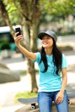 O skater da mulher senta-se usa seu telefone celular fotografia de stock royalty free O skater da mulher senta-se usa seu telefone celular fotografia de stock royalty free