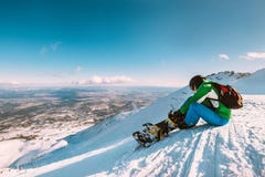O Snowboarder prende as curvaturas do snowboard que sentam-se na parte superior do monte da neve Imagens de Stock O Snowboarder prende as curvaturas do snowboard que sentam-se na parte superior do monte da neve Imagens de Stock