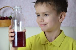 O suco bebendo do rapaz pequeno bonito em casa, suco da cereja bebe de uma garrafa ou de um vidro com uma palha fotografia de stock O suco bebendo do rapaz pequeno bonito em casa, suco da cereja bebe de uma garrafa ou de um vidro com uma palha fotografia de stock