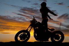 O suporte da motocicleta da mulher da silhueta entrega para trás imagem de stock O suporte da motocicleta da mulher da silhueta entrega para trás imagem de stock