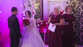 O suporte novo dos noivos no salão do casamento e no mestre de cerimônias fala palavras na parede do fundo decorada com as flores video estoque O suporte novo dos noivos no salão do casamento e no mestre de cerimônias fala palavras na parede do fundo decorada com as flores video estoque