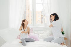 O tiro horizontal da mãe nova satisfeito e de sua luta pequena da filha com os descansos na cama, tem as expressões felizes, inse foto de stock O tiro horizontal da mãe nova satisfeito e de sua luta pequena da filha com os descansos na cama, tem as expressões felizes, inse foto de stock